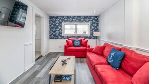 Een gezellige, compacte woonkamer met een rode bank, een klein bijzettafeltje en een aan de muur bevestigde televisie.