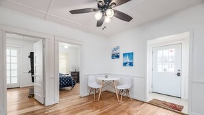 Een kamer met houten vloer, een plafondventilator, een eettafel met stoelen en een deur met deurmat.