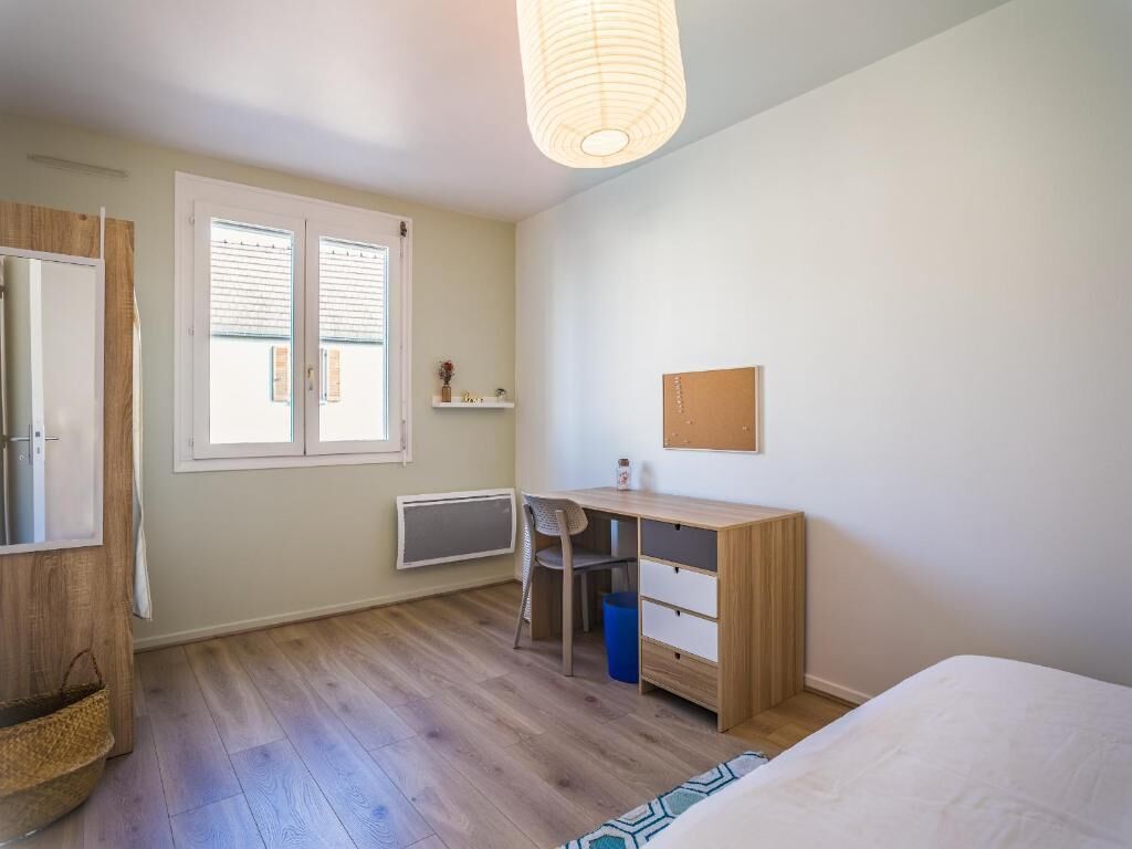 Un dormitorio con cama, escritorio, silla, radiador y ventana con persianas.