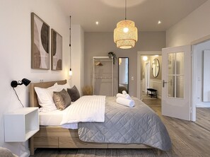 Een moderne slaapkamer met een bed, nachtlampjes, een hanglamp, een kledingkast en een spiegel.
