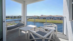 Ein Balkon mit Blick auf ein Gewässer und Gebäude. Weiße Möbel und ein Geländer sind vorhanden.