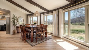 Ein Essbereich mit Holztisch und Stühlen, großen Fenstern und Blick ins Freie.