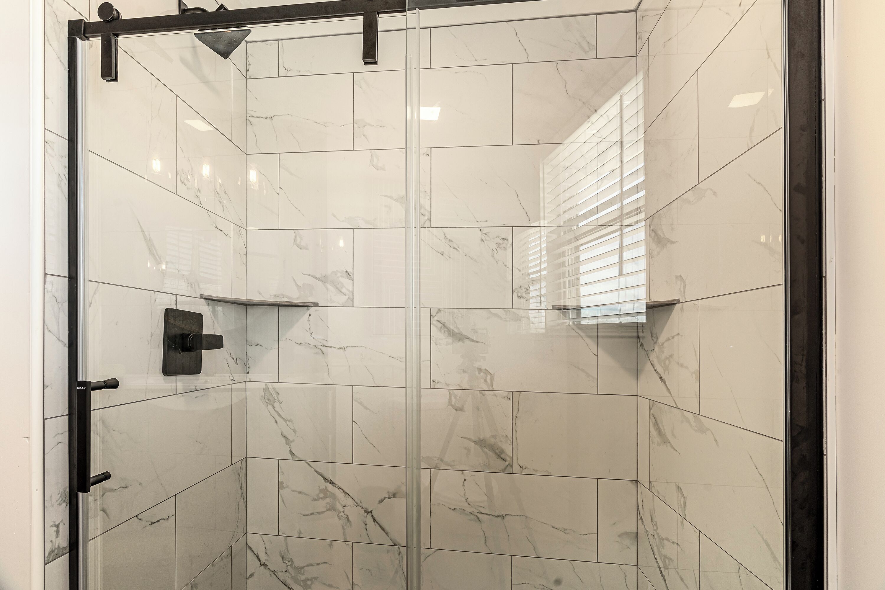 A glass-enclosed shower with white marble tiles and a black faucet.