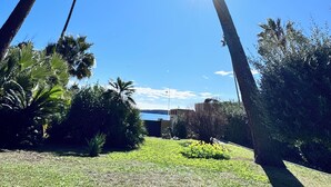 A garden with tall trees, a clear blue sky, and a building in the background. - VILLA PALM BEACH sea front  (cannes)