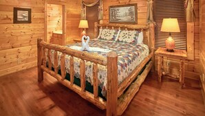 A wooden cabin-style bedroom with a bed, two lamps, a ceiling fan, and a framed picture on the wall.