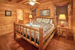 Une chambre à coucher de style cabane en bois, avec un lit, deux lampes, un ventilateur de plafond et un tableau encadré au mur.