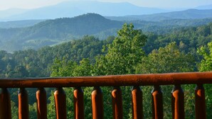 A view of a forested mountain range from a balcony with a metal railing.