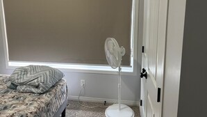 Une chambre à coucher avec un lit, un ventilateur sur pied, une fenêtre et une porte.