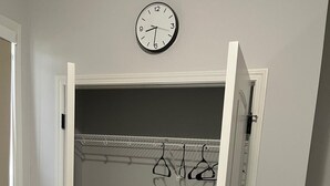 Une pièce avec une porte blanche, une horloge murale, un portant à vêtements et un ventilateur.