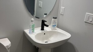 Une salle de bain avec un lavabo blanc, un robinet noir, un miroir au-dessus du lavabo et des toilettes sur la gauche.