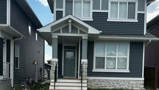 Une maison à deux étages avec un porche à l’avant, une allée et une pelouse.
