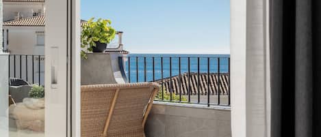A balcony with wicker furniture, a potted plant, and a view of the sea.
