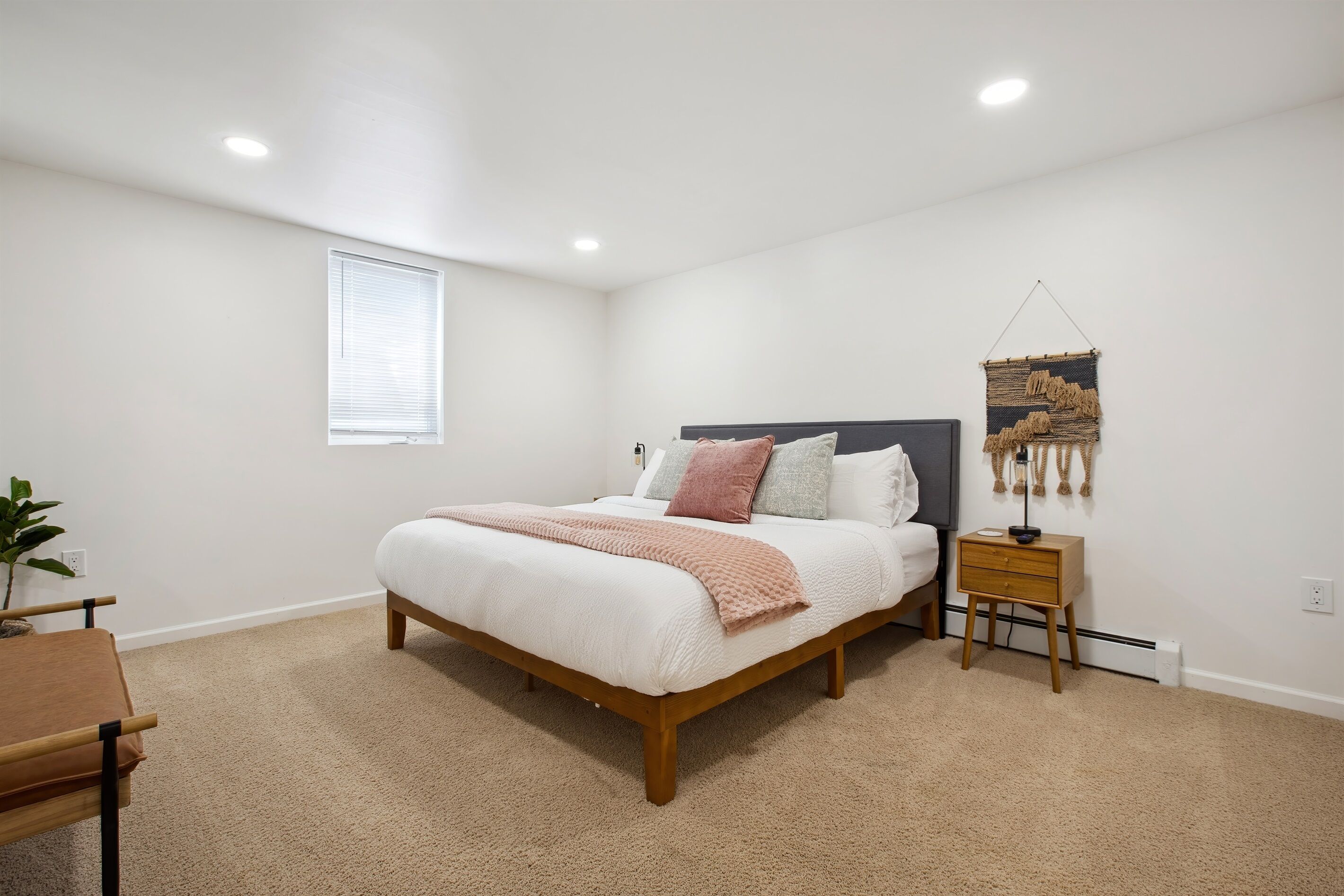 A bedroom with a bed, bedside table, lamp, and a wall-mounted tapestry.