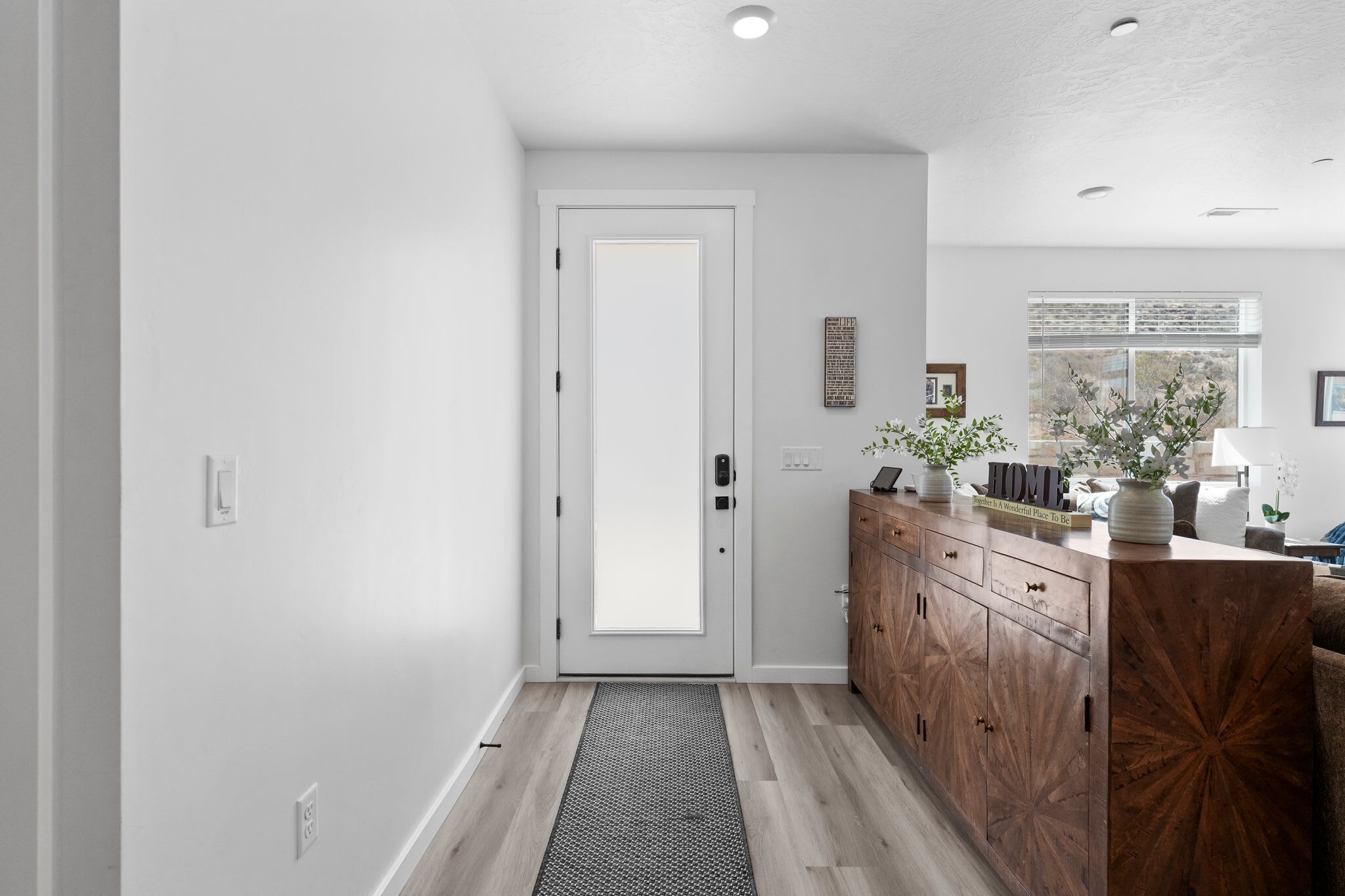 A hallway with a wooden cabinet, a white door, and a window with blinds.