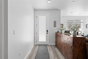 Un couloir avec une armoire en bois, une porte blanche et une fenêtre avec des stores.