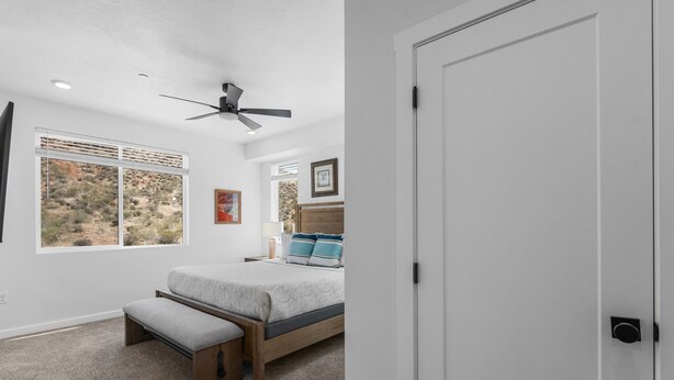 A bedroom with a bed, a bench, a ceiling fan, and a window with a desert view.
