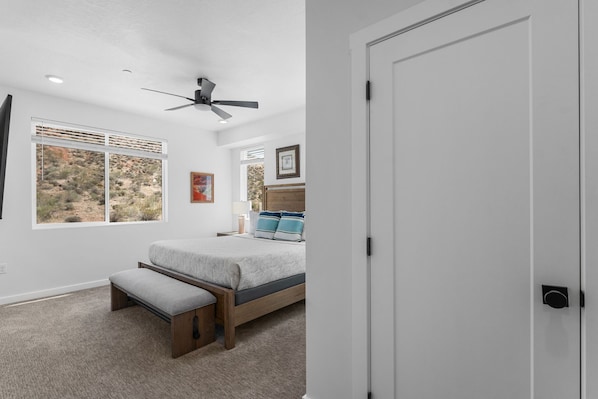 A bedroom with a bed, a bench, a ceiling fan, and a window with a desert view.