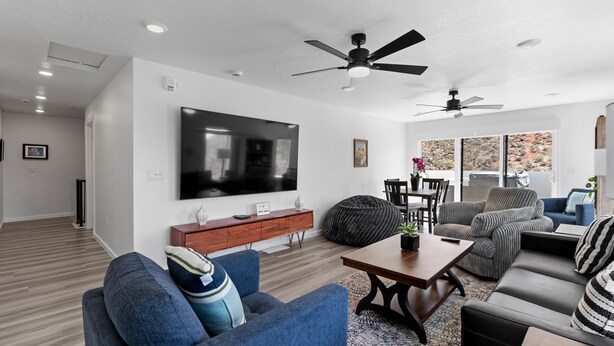 A modern living room with a flat-screen TV, sofas, a coffee table, and ceiling fans. - Touch of Class - 5BR - Private Hot Tub & Near Zion (Hurricane)