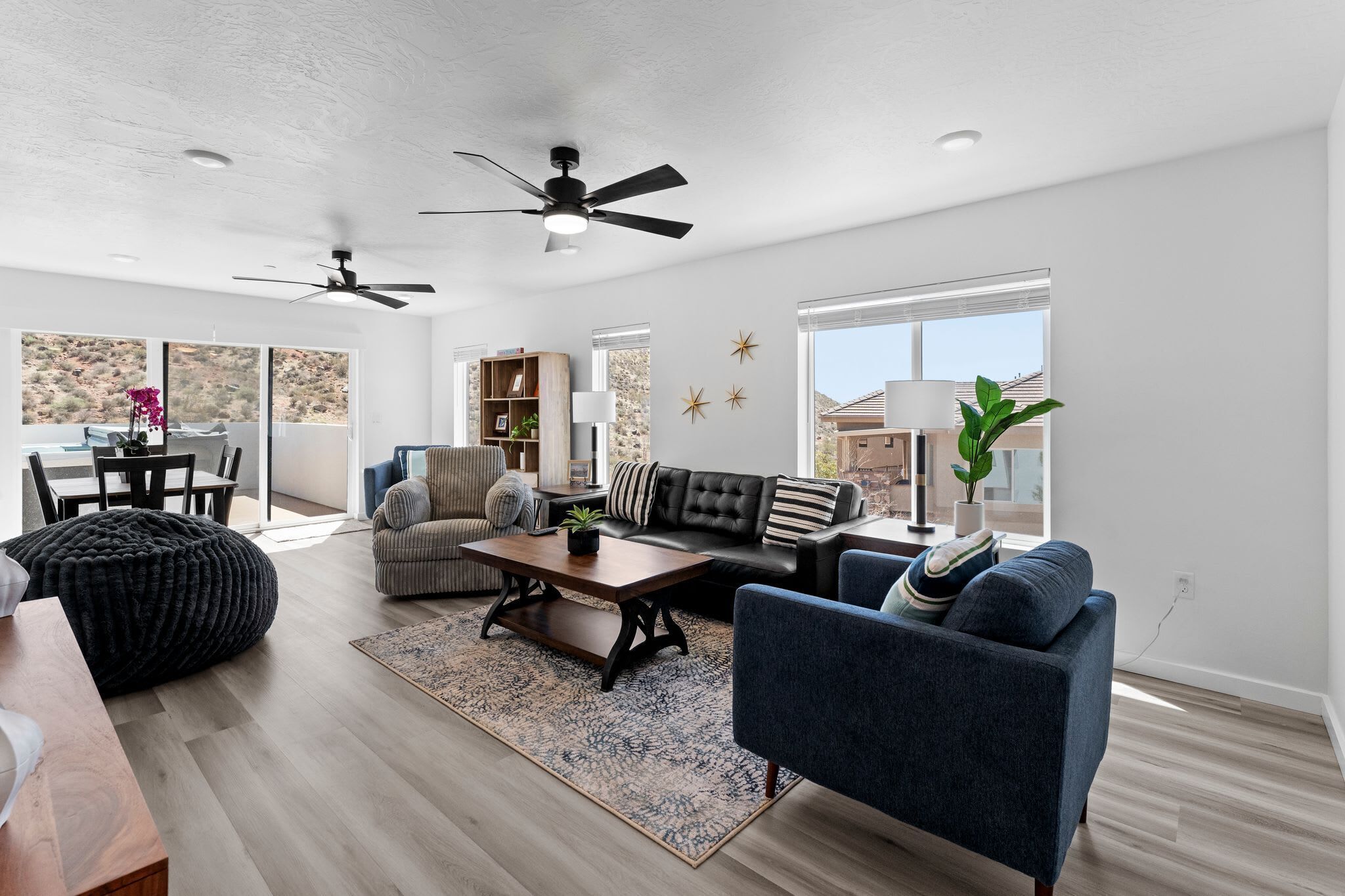 A modern living room with a sofa, armchair, and coffee table, a dining area with a table and chairs, and a large window with a view of a mountainous landscape.