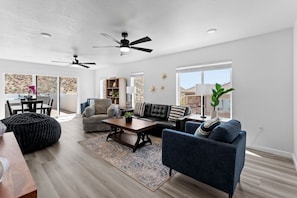 Un salon moderne comprenant un canapé, un fauteuil et une table basse, un coin repas avec une table et des chaises, et une grande fenêtre offrant une vue sur un paysage montagneux.