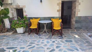 Une terrasse extérieure avec un sol en pierre, deux chaises en bois, une petite table ronde et un pot de fleurs orné de fleurs roses.