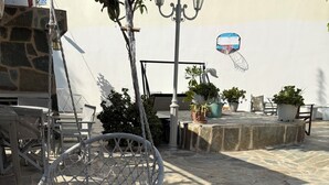 A stone-tiled patio with a hanging chair, outdoor furniture, and potted plants. - GARDEN APARTMENT (ELECTRIC CAR CHARGING STATION) (North Kynouria)