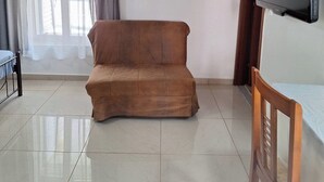 A living room with a brown sofa, a TV mounted on the wall, a framed picture, and a window with curtains. - GARDEN APARTMENT (ELECTRIC CAR CHARGING STATION) (North Kynouria)