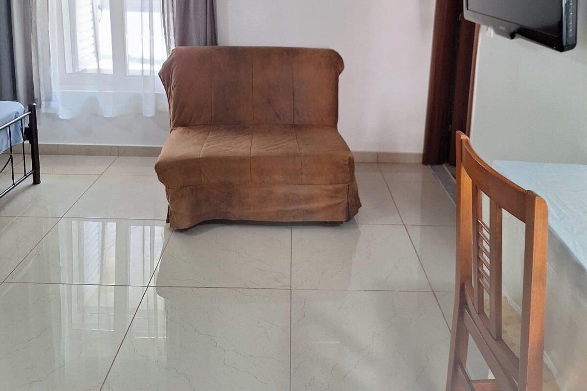 Una sala de estar con un sofá marrón, un televisor montado en la pared, un cuadro enmarcado y una ventana con cortinas.