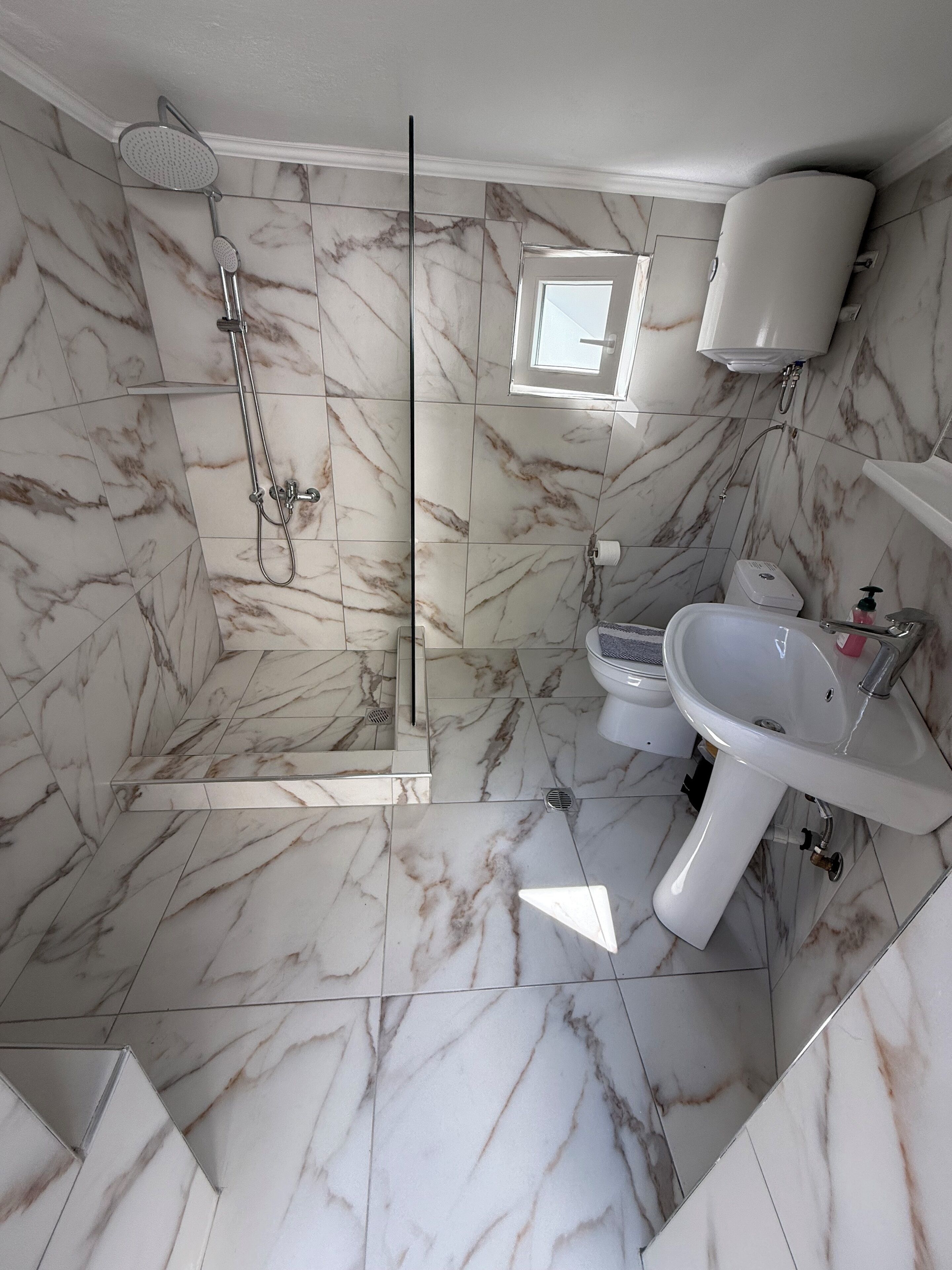 Ein Badezimmer mit Marmorböden, einer gläsernen Duschkabine, einem Waschbecken und einer Toilette.