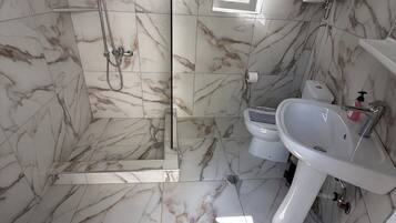 Ein Badezimmer mit Marmorböden, einer gläsernen Duschkabine, einem Waschbecken und einer Toilette.
