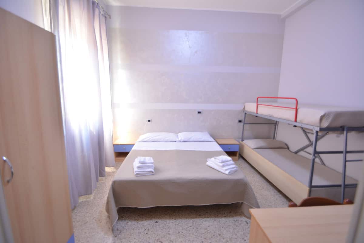 Habitación de hotel con una cama individual, una cama litera, una puerta de madera y una cortina.