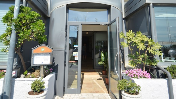 A modern building with a curved entrance, a flag, and potted plants. - HOTEL  BELLA ROMAGNA     (Ravenna)