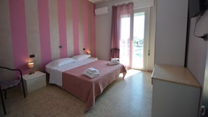 A bedroom with a bed, bedside tables, a chair, a TV, and a window with curtains. - HOTEL  BELLA ROMAGNA     (Ravenna)