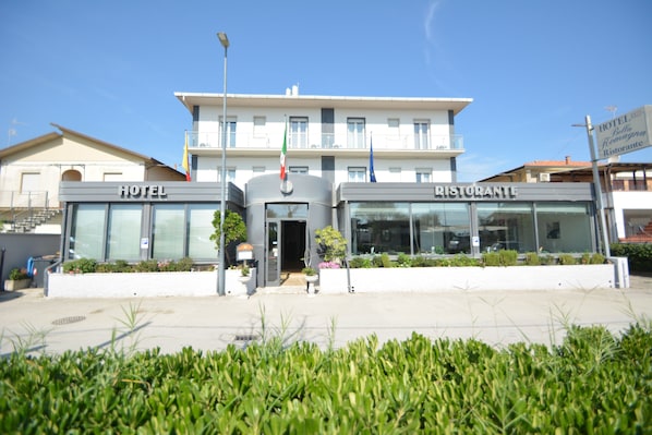Un hôtel et un restaurant dotés d’une façade moderne, de grandes fenêtres et d’un drapeau.