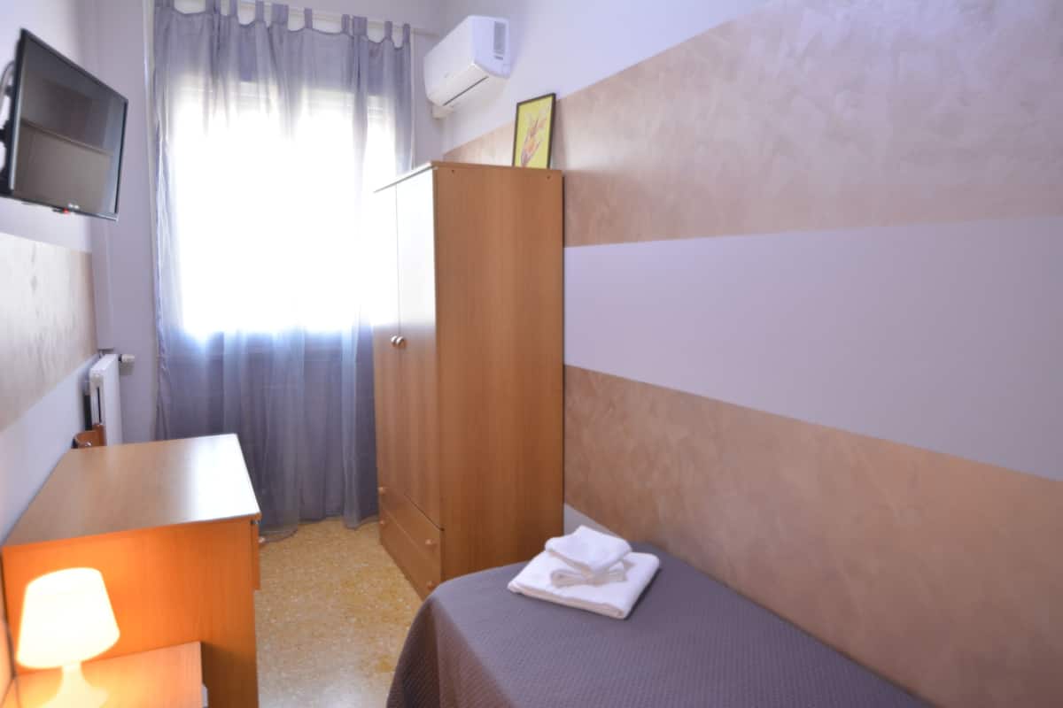 Habitación de hotel con cama, escritorio con lámpara, armario y televisor fijado a la pared.