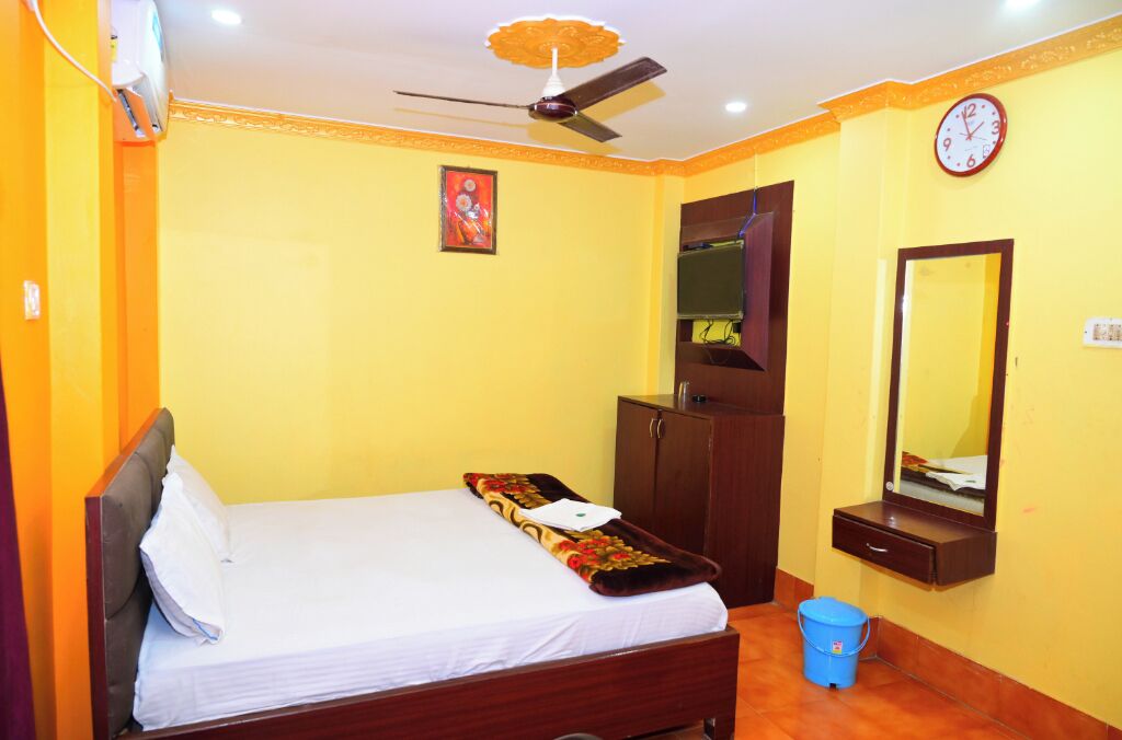 A bedroom with a bed, a ceiling fan, a wardrobe, a mirror, and a clock on the wall.