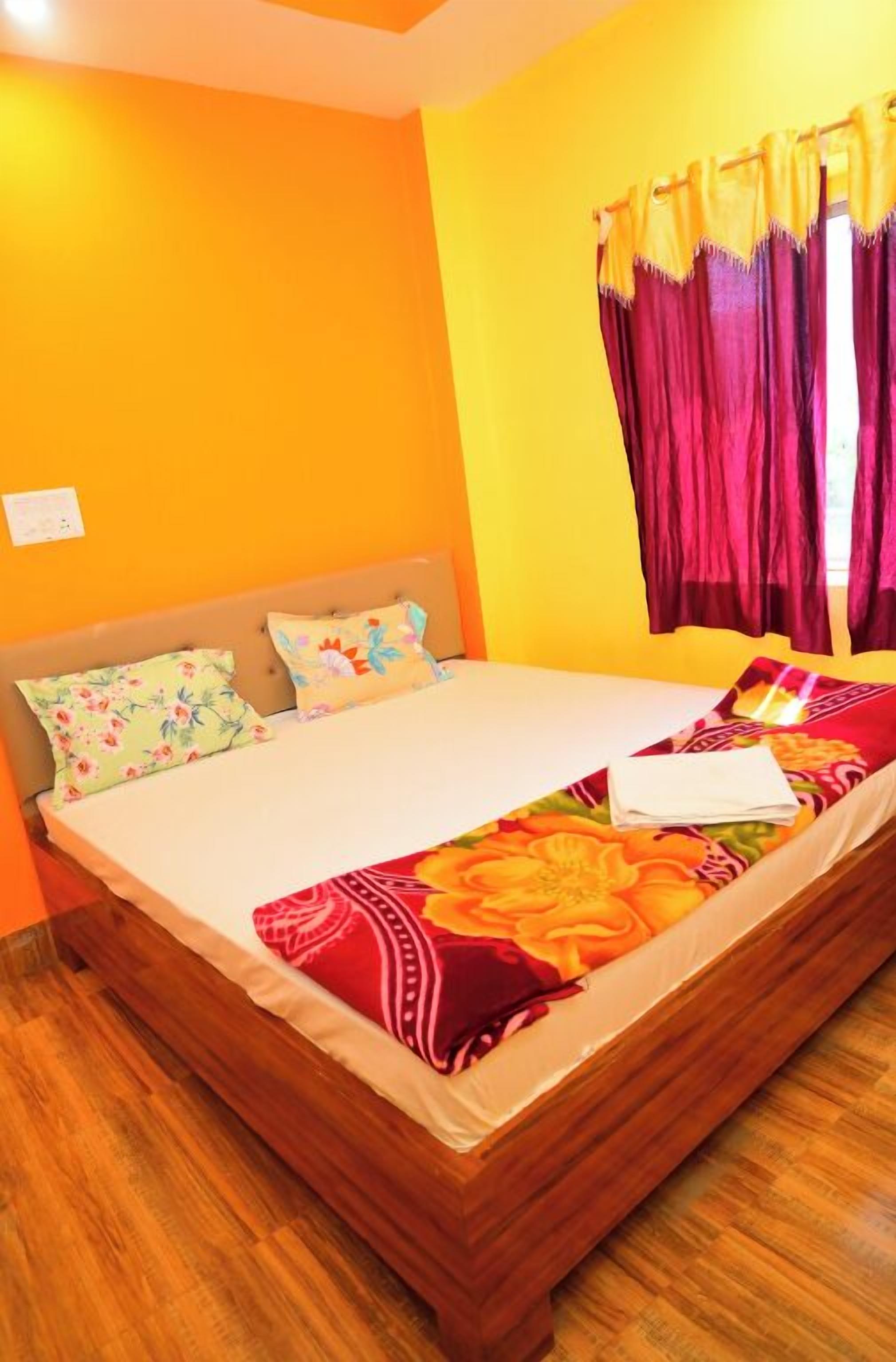 Ein Einzelbett mit einer blumigen Tagesdecke, zwei Kissen und einem Holzkopfstück in einem Zimmer mit orangefarbenen Wänden und einem Fenster mit violetten Vorhängen.