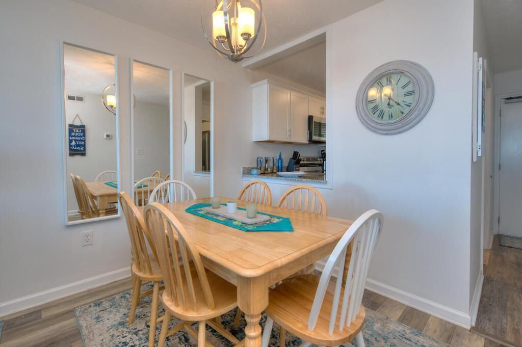Een eetruimte met een houten tafel en stoelen, een kroonluchter en een klok aan de muur.
