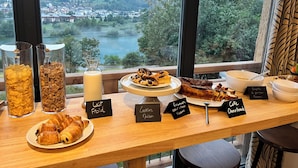 A breakfast buffet with croissants, cookies, and a view of a lake and mountains. - La Grange des Eulets (Bourg-Saint-Maurice)