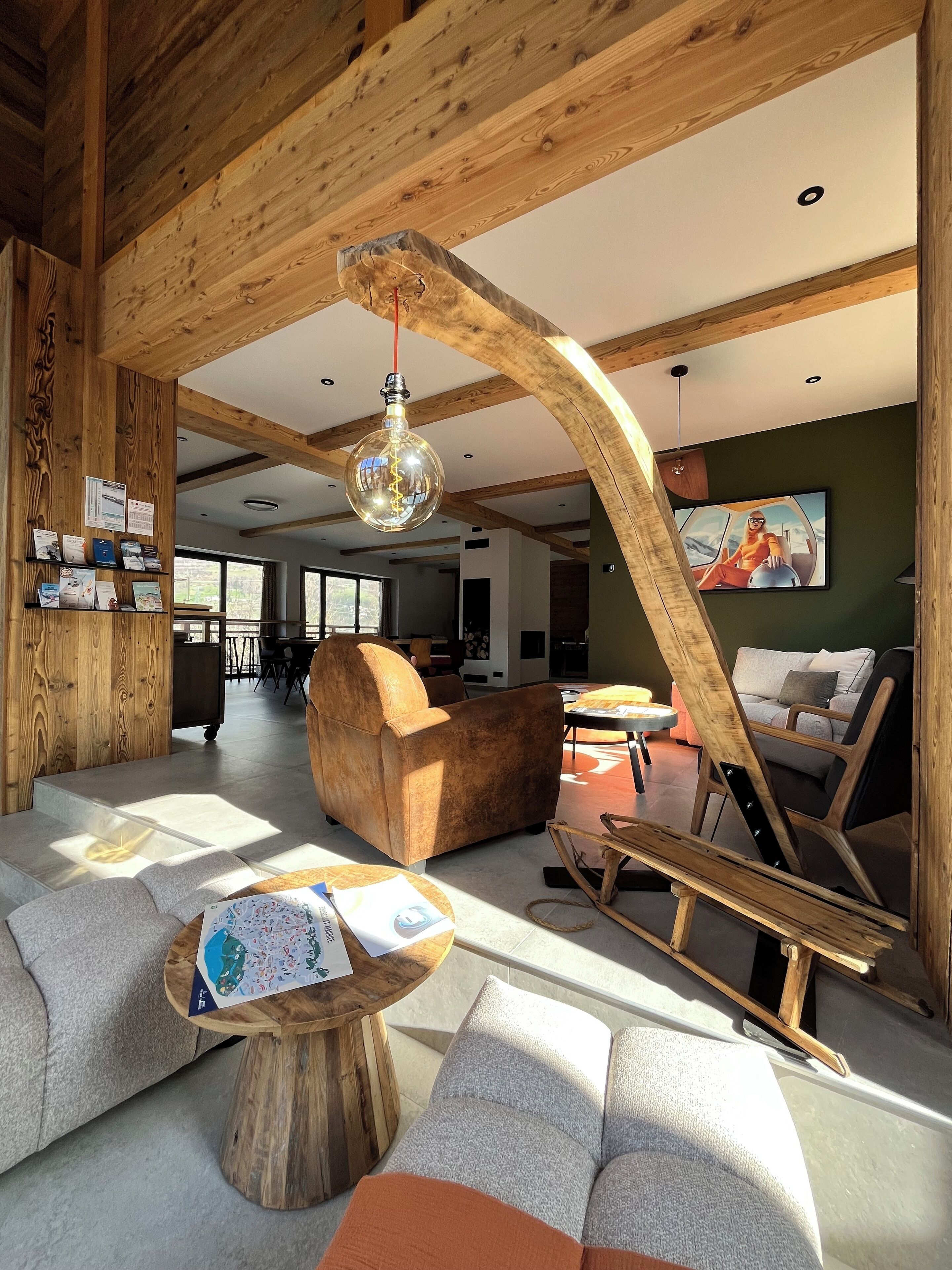 A spacious living area with a high ceiling, wooden beams, a large armchair, a sofa, a wooden coffee table, and a painting on the wall.