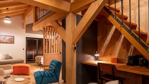 A spacious living area with a wooden staircase, a blue armchair, a gray sofa, and a small table with a remote control. - La Grange des Eulets (Bourg-Saint-Maurice)