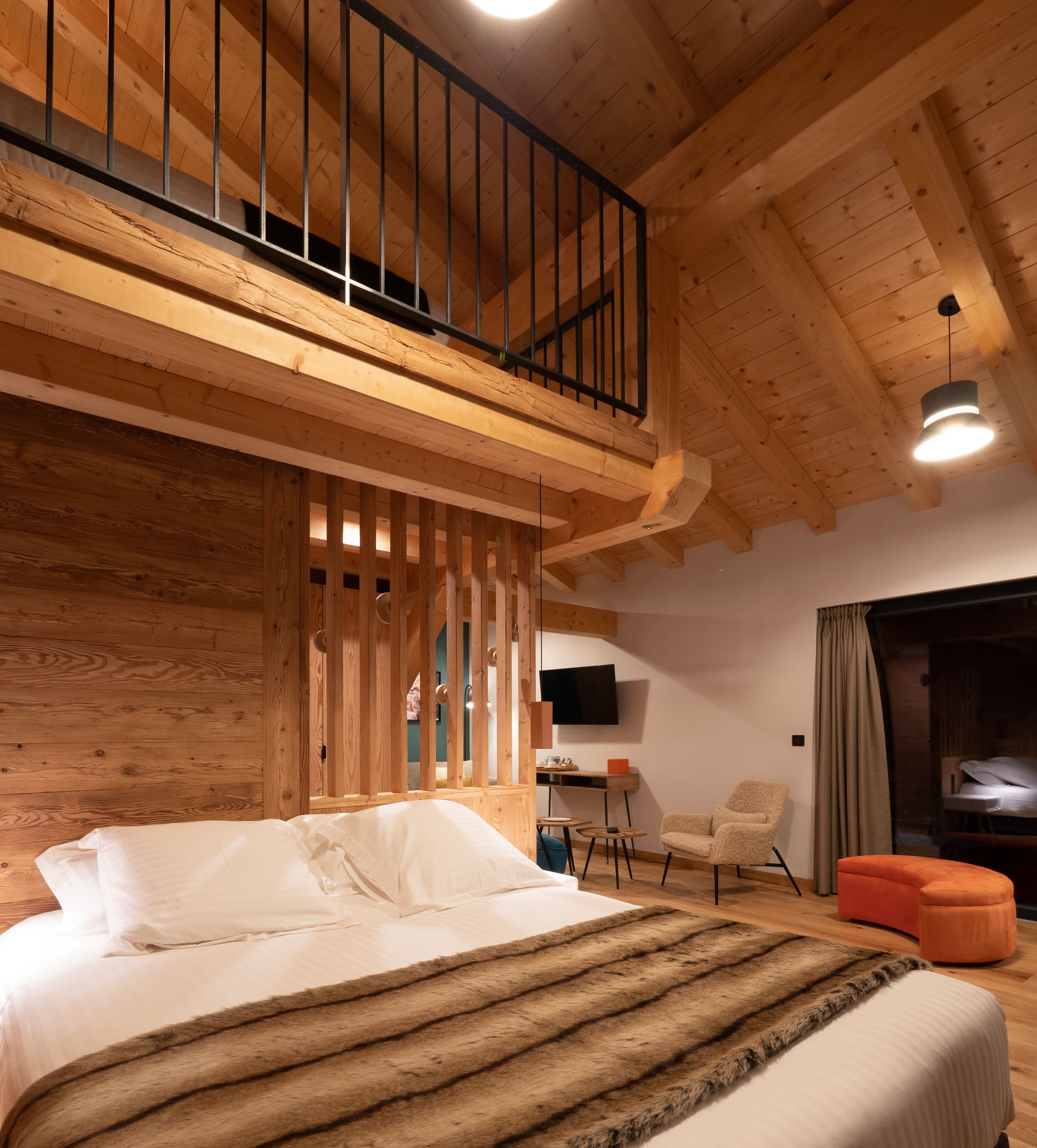 Un dormitorio con una cama grande, techo de madera, balcón, escritorio, silla y sofá.