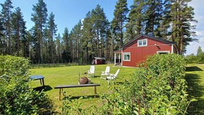 A red cabin with a grassy yard, white chairs, and a bench. - Lapland Pure Nature and More! (Bastutrask)