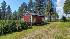 A red wooden cabin with a metal roof, surrounded by a forest and a gravel path. - Lapland Pure Nature and More! (Bastutrask)