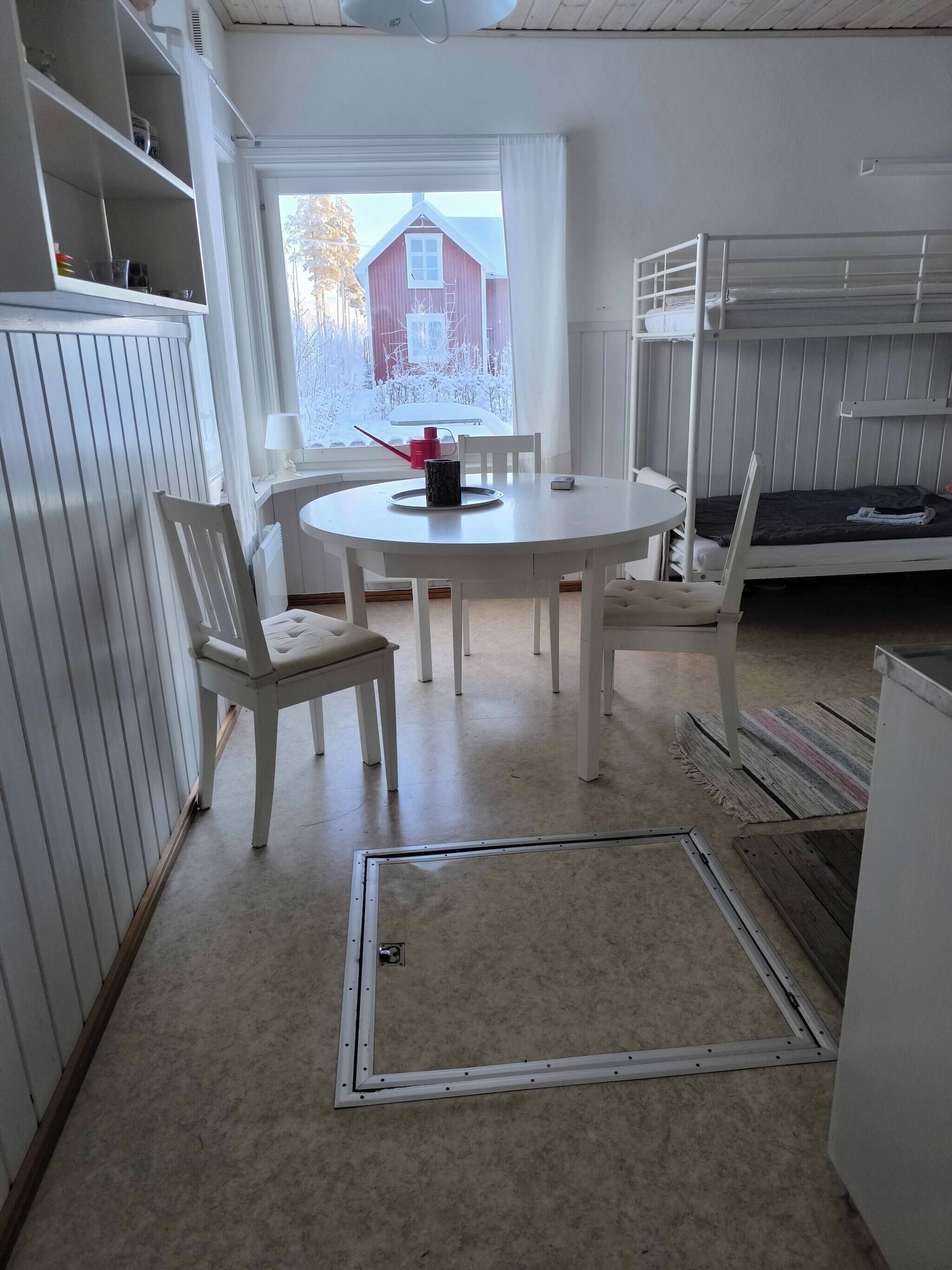 Une pièce avec une table à manger blanche, des chaises, un lit superposé et une vue sur un bâtiment rouge à l’extérieur.