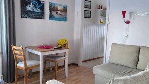 A modern living room with a wooden floor, a white sofa, a dining table with chairs, and two wall-mounted paintings. - Lapland Pure Nature and More! (Bastutrask)