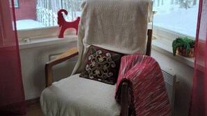 A cozy chair with a blanket, a cushion, and a view of a snowy forest through a window. - Lapland Pure Nature and More! (Bastutrask)