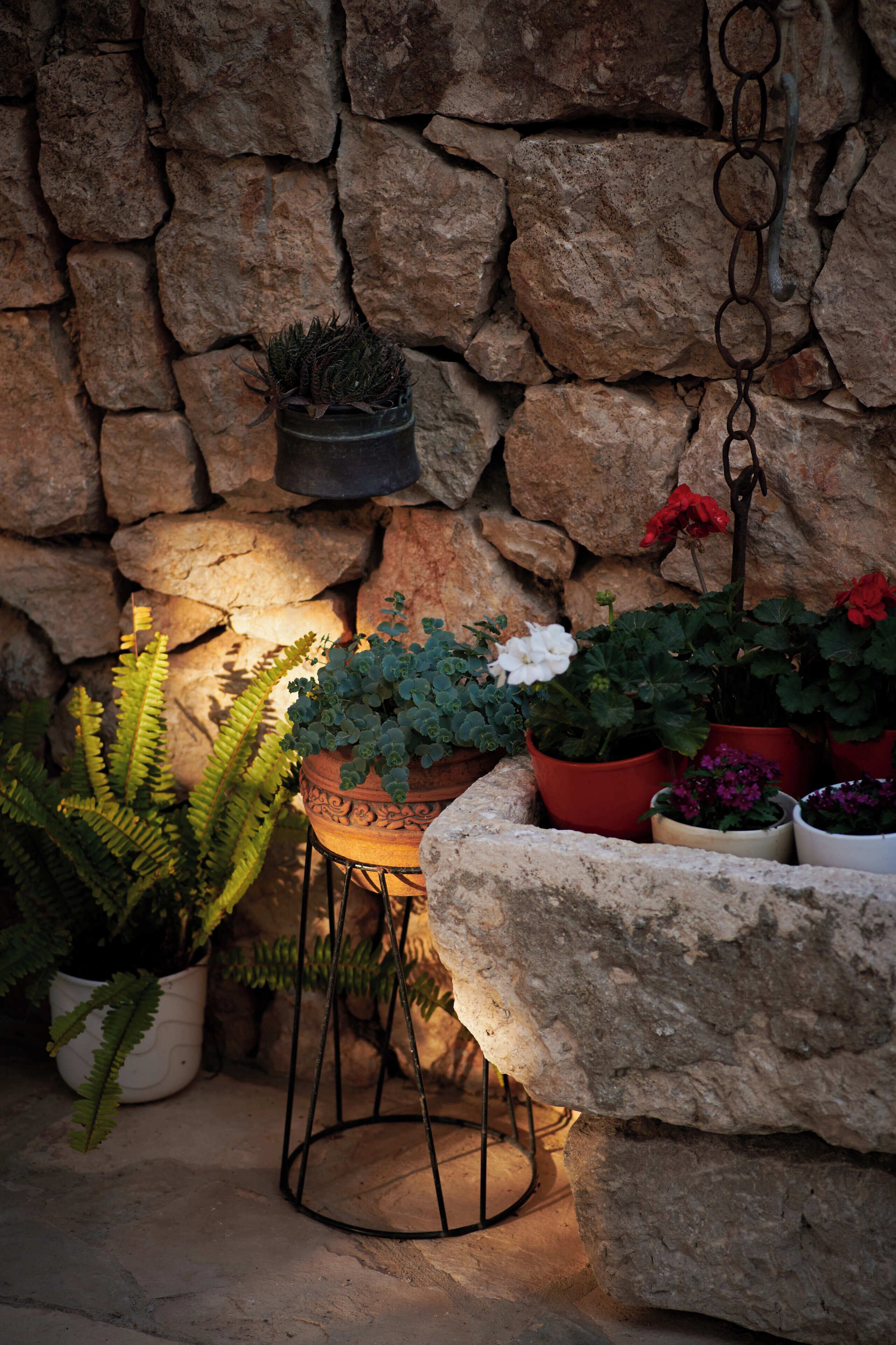 Un muro de piedra con plantas en macetas y un objeto metálico colgante.