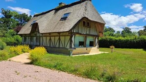 A traditional half-timbered house with a thatched roof, surrounded by a well-maintained garden and a gravel path leading to the entrance.