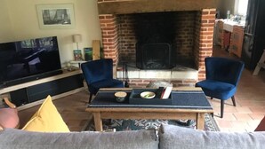 A living room with a brick fireplace, a TV, and two blue chairs.